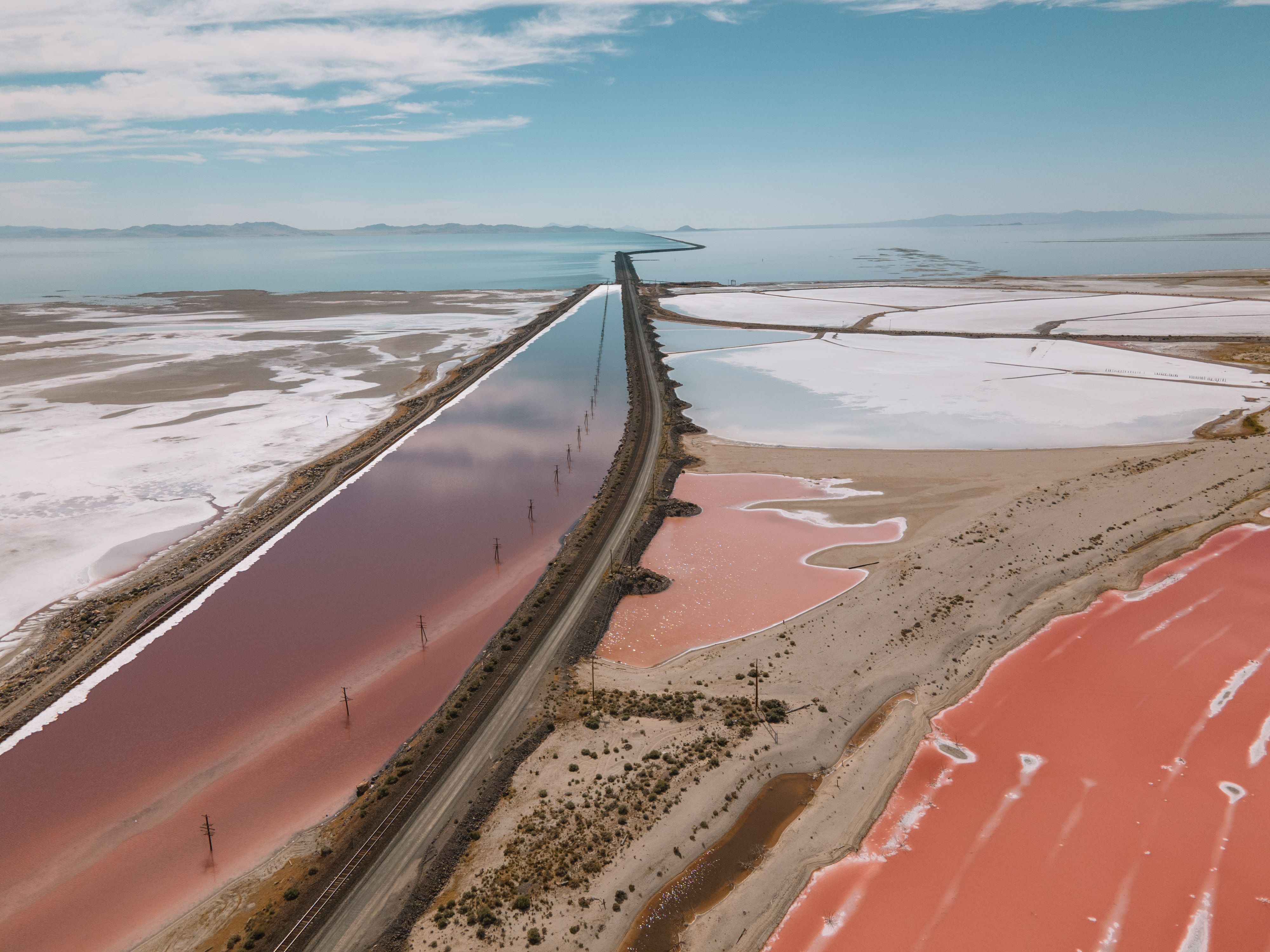 Aerial view of exposed white salt flats and pink mineral evaporation ponds along the Great Salt Lake, split by a rail causeway